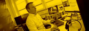 Glücklicher Mann sitzt am Schreibtisch und arbeitet mit der maja.cloud